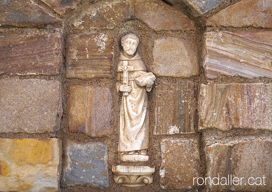 Escultura encastada a la paret d'un sant amb una creu i un llibre.